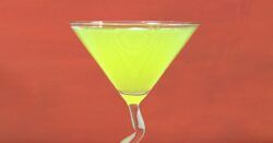 Bright yellow Algonquin Cocktail in front of dark orange background