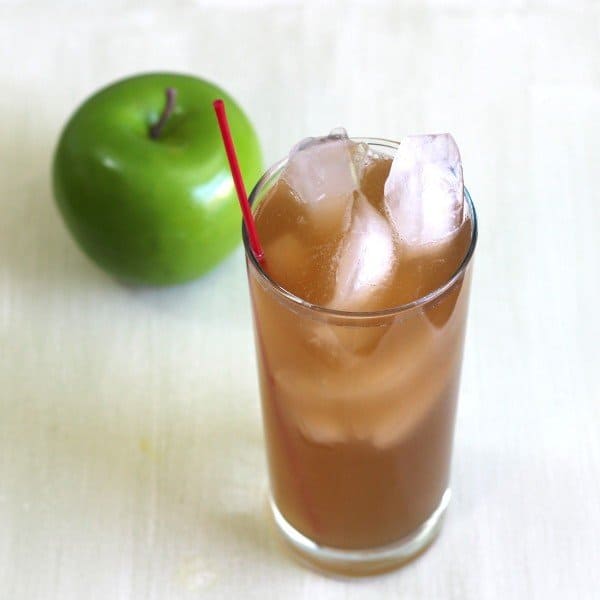 Angled view of Apple Cart drink in tall glass with ice beside apple