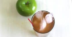 Apple Cart drink in tall glass with ice beside apple