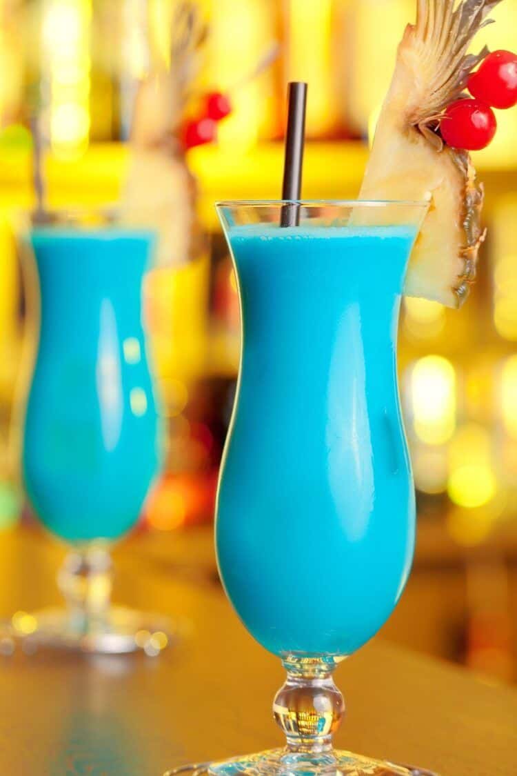 Two Blue Hawaiian drinks on bar in hurricane glasses