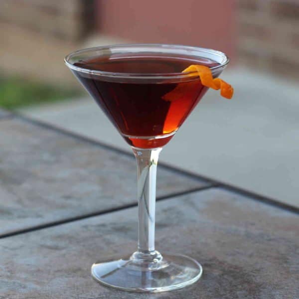 Boulevardier drink with orange twist on patio table with brick wall background