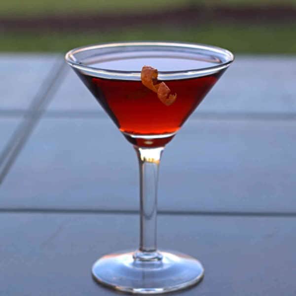 Closeup of Boulevardier drink with orange twist on patio table