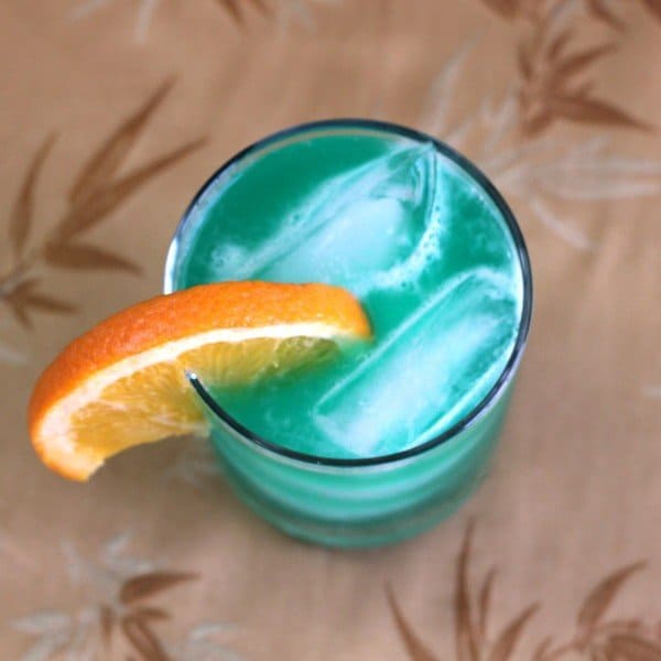 Overhead view of bright teal Chameleon drink with orange slice