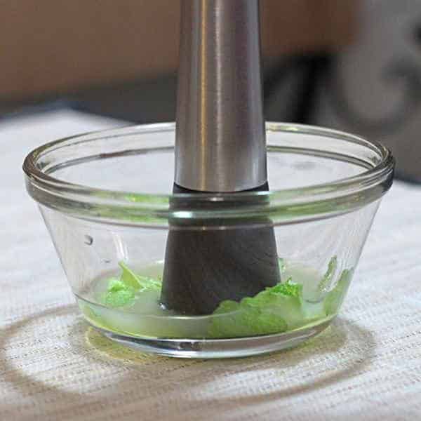 Side view of cocktail muddler crushing mint leaves