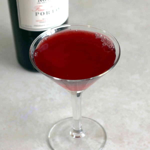 Angled view of Crimson Cocktail in front of bottle of port
