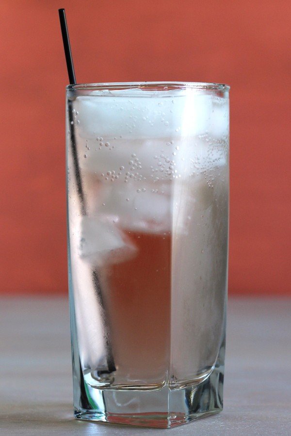 Even Pair drink in tall glass with ice in front of red backdrop