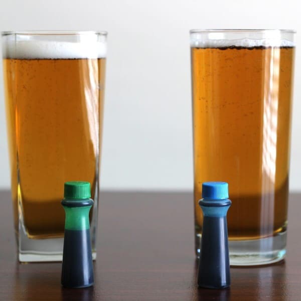 Two glasses of beer with green and blue food coloring droppers in front of them