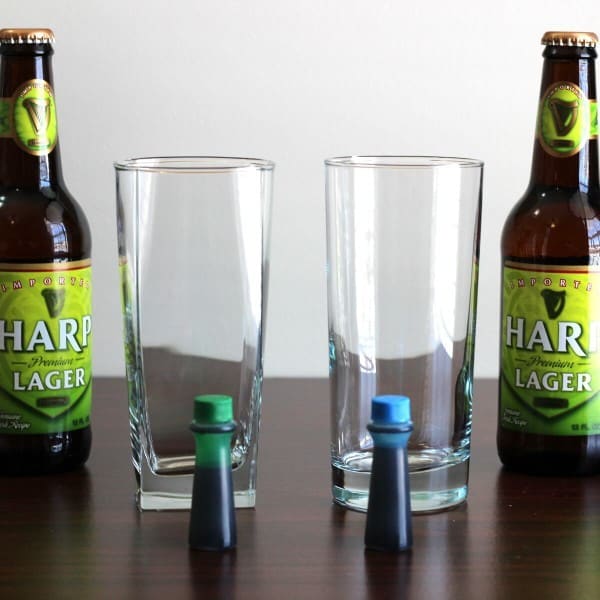 Two bottles of beer beside two glasses with green and blue food coloring droppers