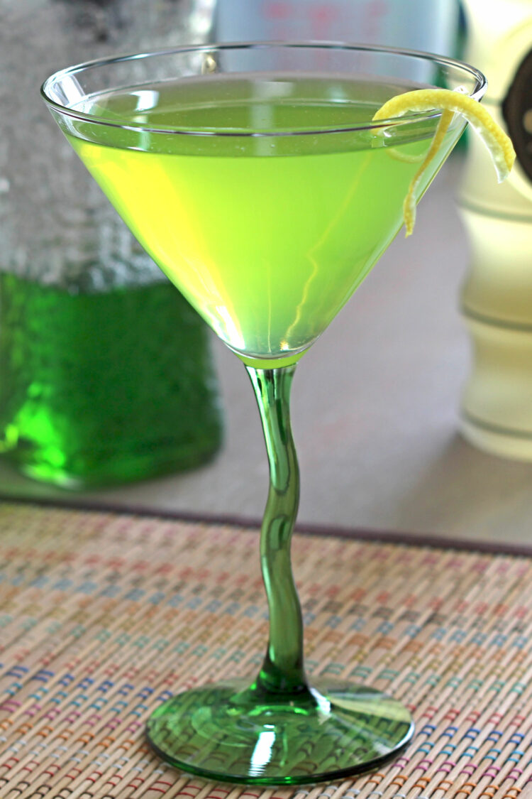 Bright green cocktail in martini glass with lemon twist