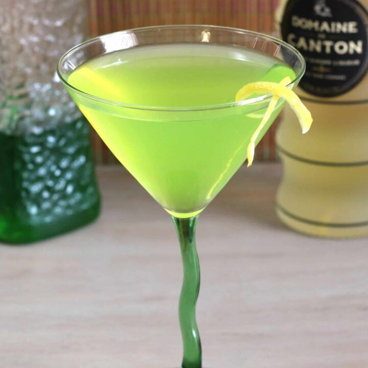 Bright green cocktail in martini glass with lemon twist