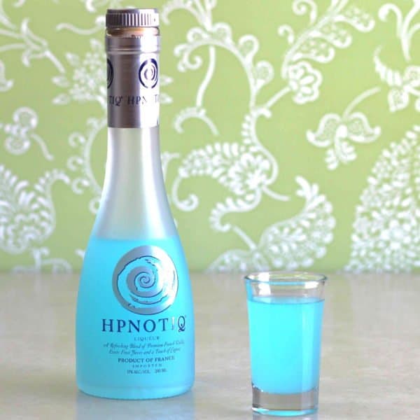 Hpnotiq bottle next to show glass of same with green background