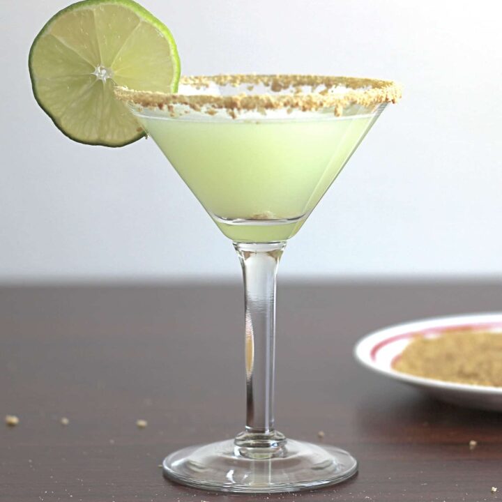 Pale green Key Lime Martini in glass with lime wheel and graham cracker crumb rim