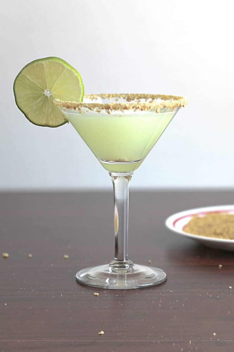 Pale green Key Lime Martini in glass with lime wheel and graham cracker crumb rim