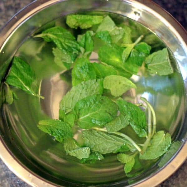 Overhead view of mint leaves soaking in bowl of water