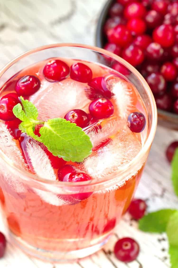 Overhead view of pinkish Mistletoe Martini cocktail with cranberries and mint leaves