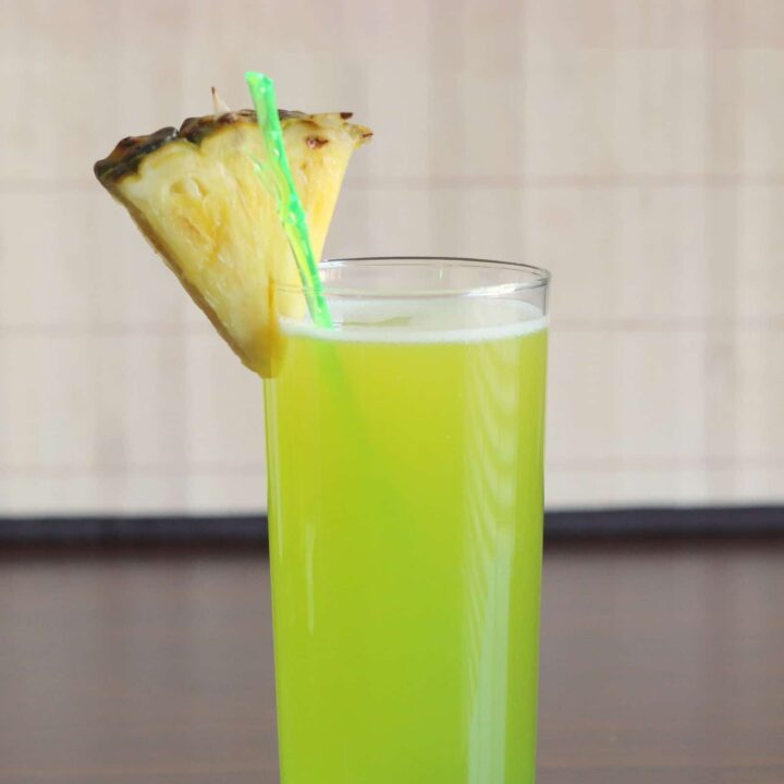 Bright green Monkey In a Tree drink with pineapple wedge garnish on table