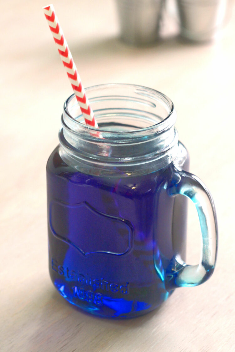 Prison Blues cocktail in mason jar glass with paper straw