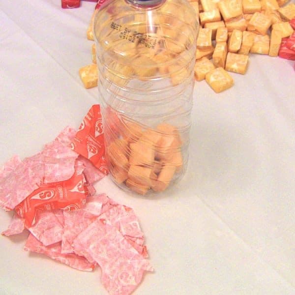 Closeup of orange starbursts in bottle with candy wrappers scattered beside bottle