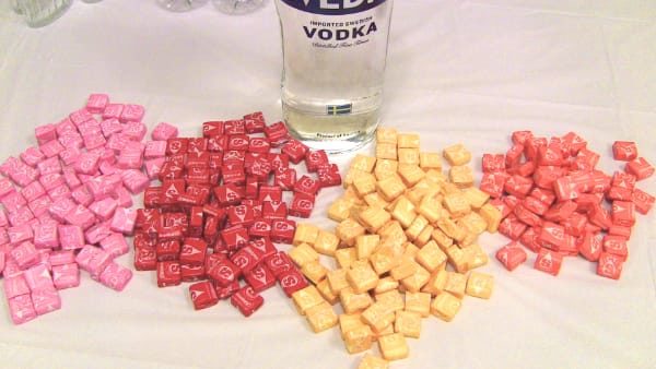Piles of Starbursts separated into flavors with bottle of vodka in background
