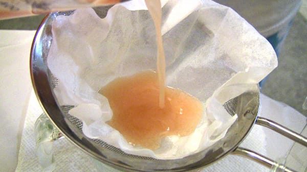 Pouring orange Starburst infusion through sieve with coffee filter