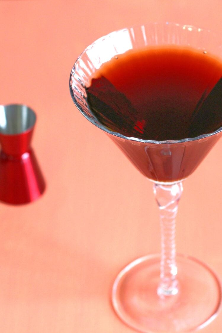 Dark brown Undertaker cocktail in tall martini glass next to red jigger