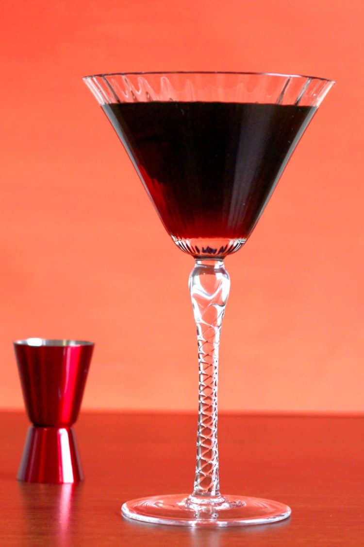 Dark brown Undertaker cocktail in tall martini glass next to red jigger